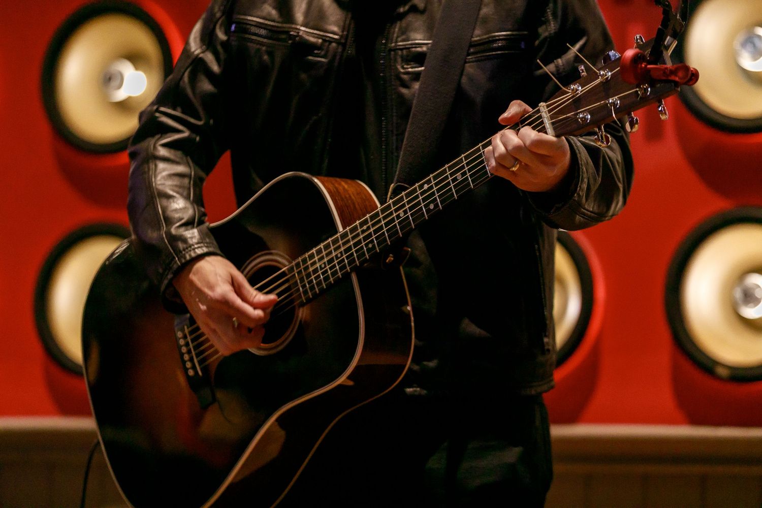Close-up of guitarist performing on stage with red and gold circular lighting pattern behind them.
