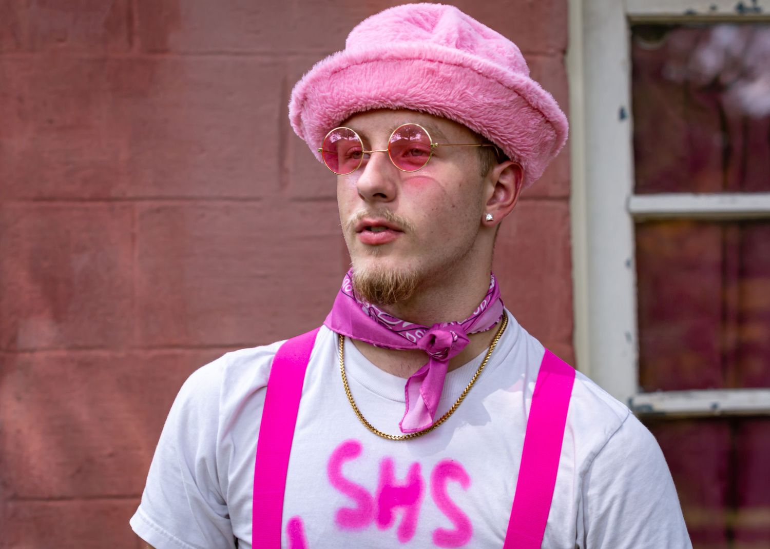 Person wearing pink bucket hat and white t-shirt with bright pink suspenders in artistic portrait series.