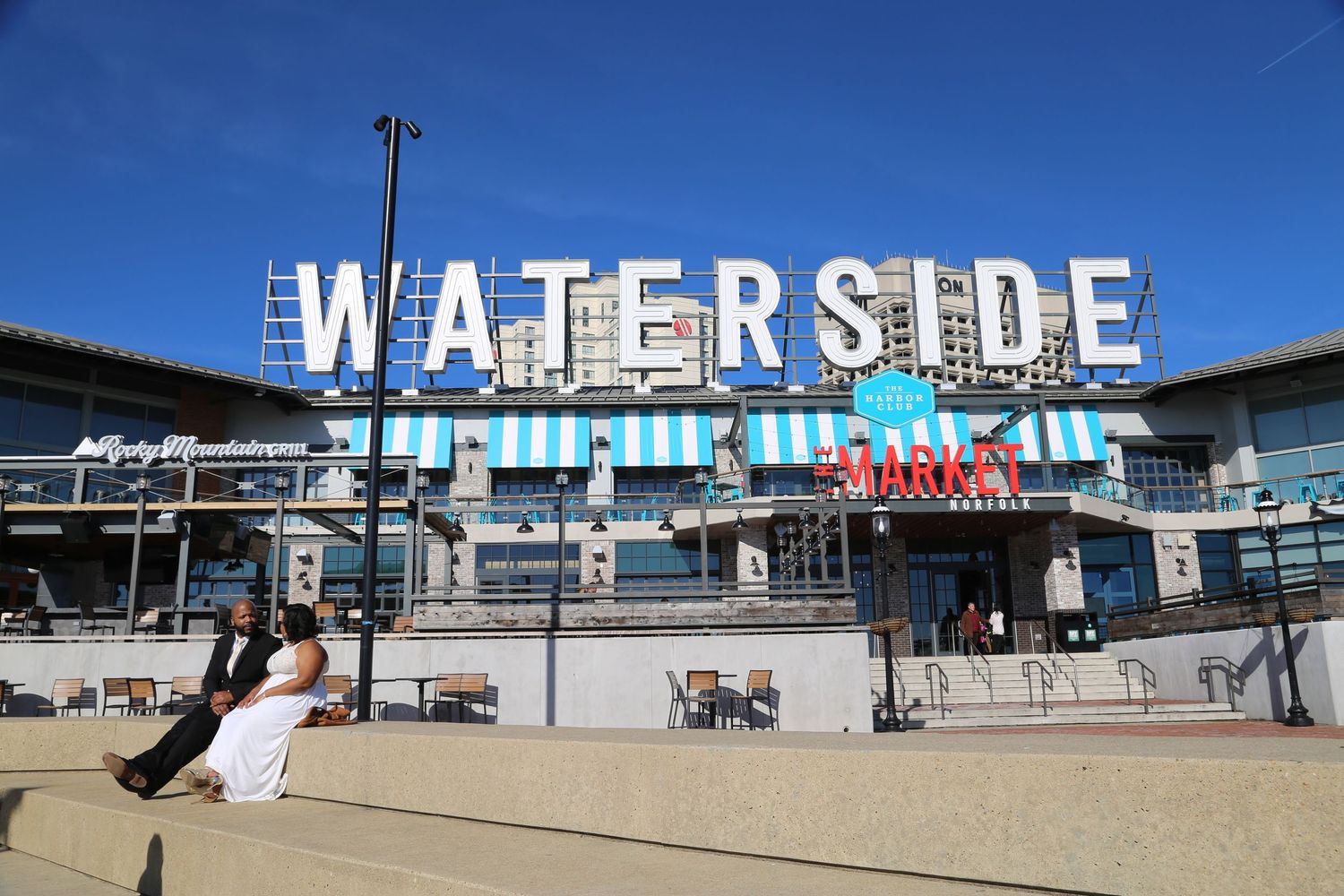 Panoramic view of Waterside waterfront retail development with outdoor walkways and seating under blue skies.