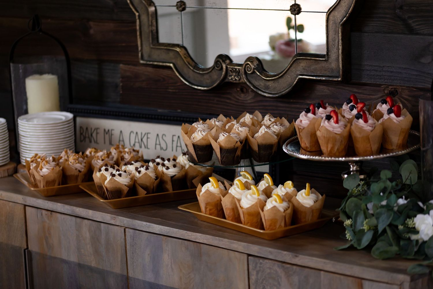 Display of various decorated cupcakes arranged on rustic wooden shelving.