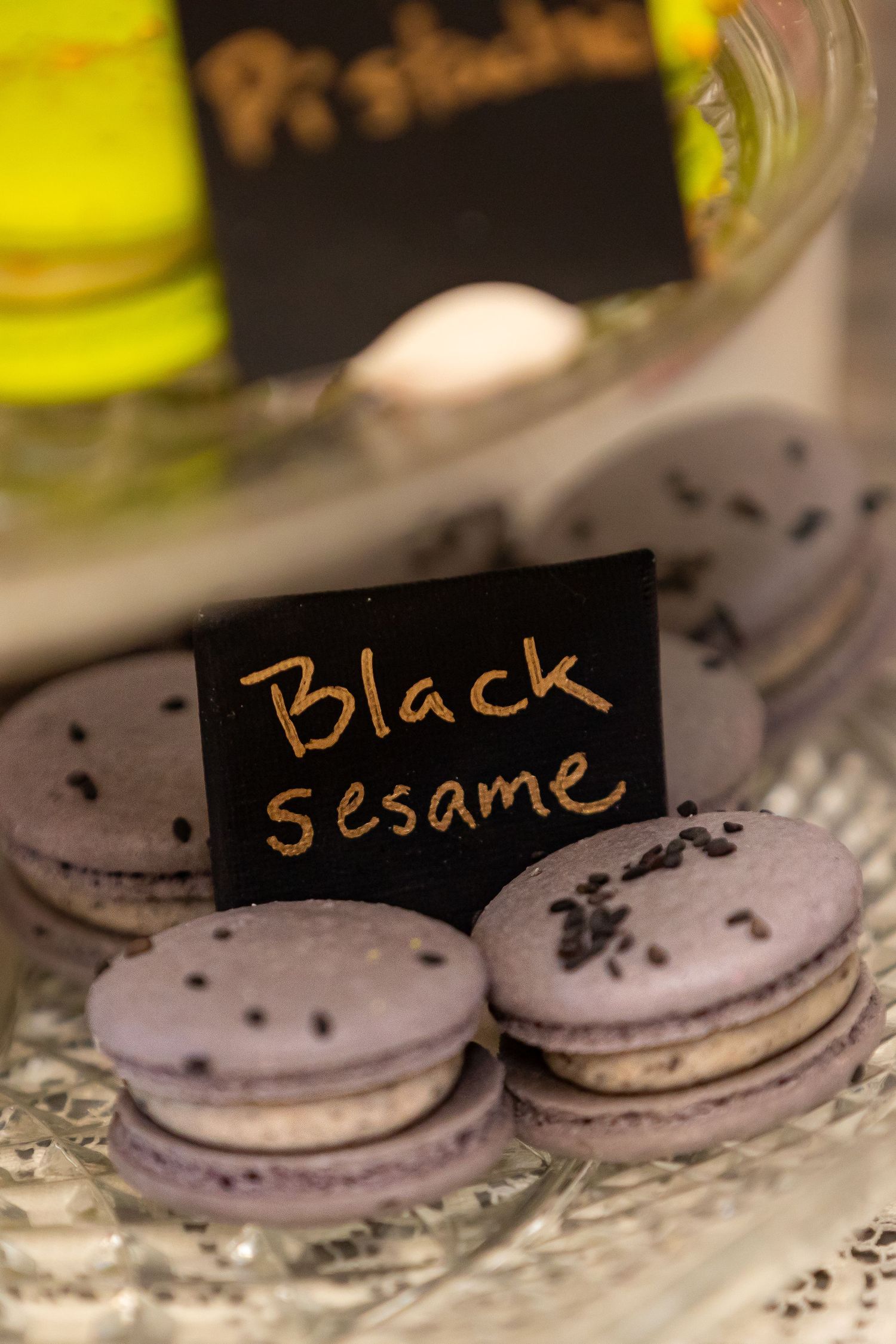 Black sesame macarons with dark sprinkles displayed on a glass serving platter with name tags.