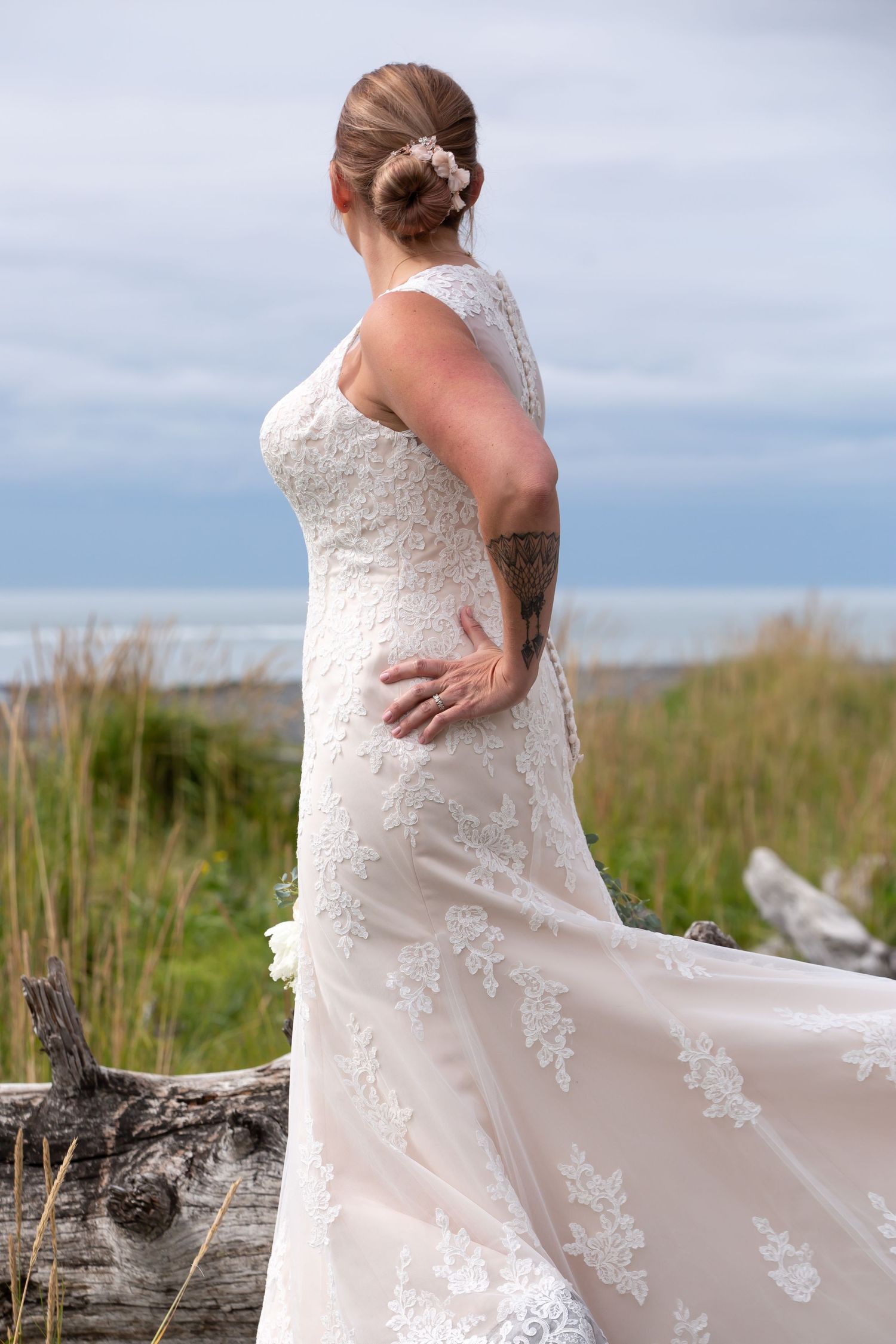 Bride in lace wedding dress poses against coastal landscape.