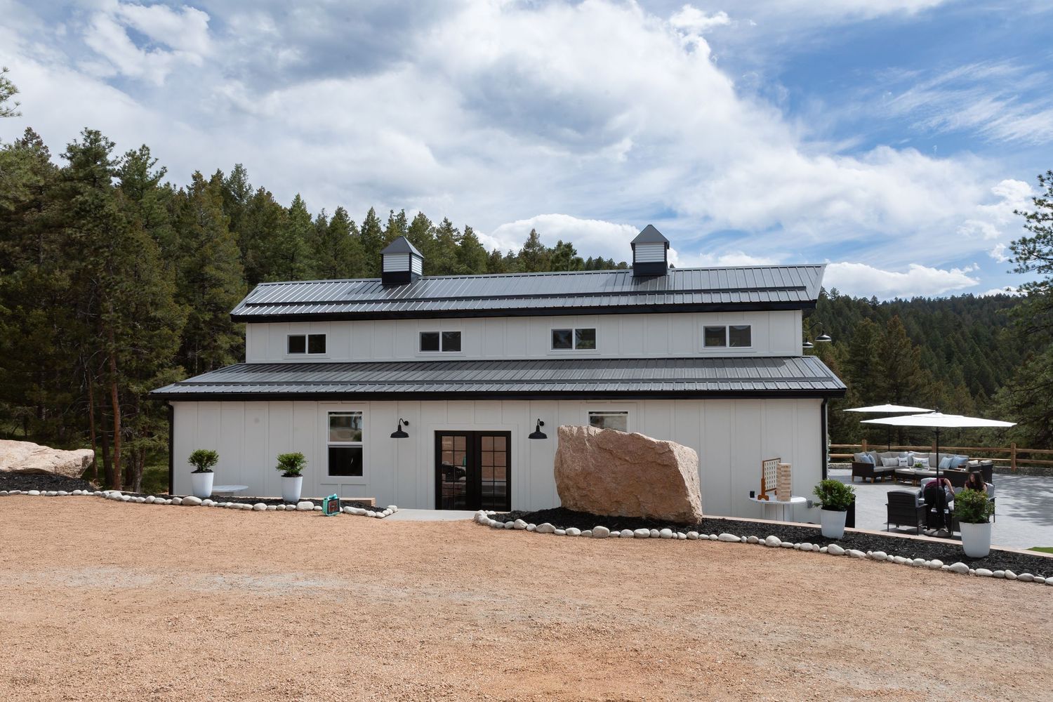 Large white barn-style building with black trim and stone accents in mountain setting.
