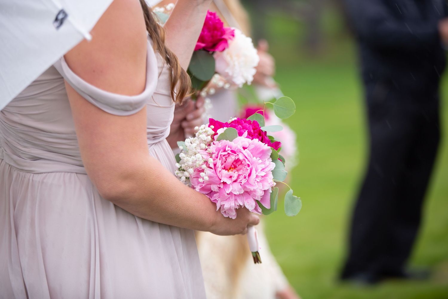 Pink and white wedding bouquets held by attendants in neutral dresses.