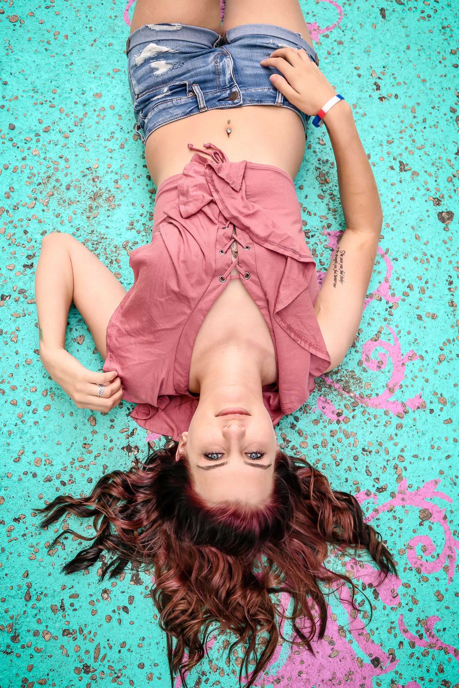 Creative portrait on turquoise floor with scattered pink paint splatter effects.
