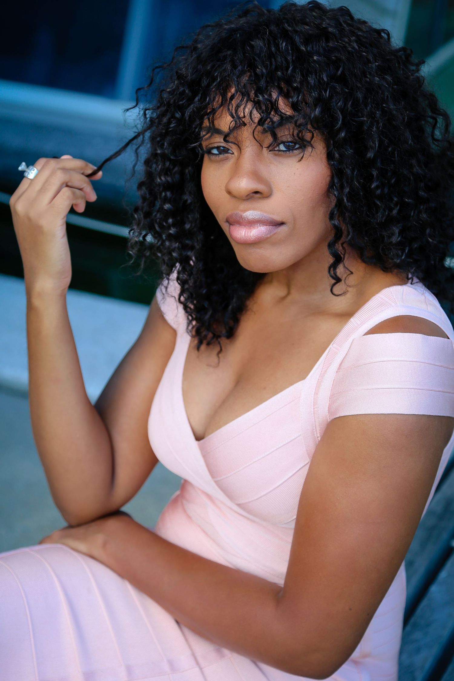 Portrait of a person in a pink dress with curly hair against a blue background.
