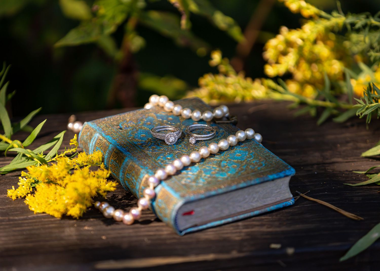 Vintage blue book with pearl necklace and yellow flowers on dark wooden surface.