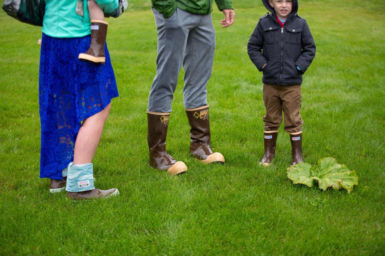 A row of dress shoes and boots stand on wet grass during an outdoor event.
