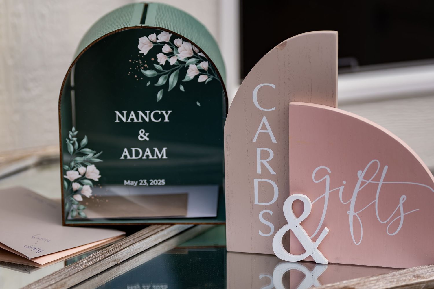 Elegant wedding signage with floral designs in dark green and blush pink colors.