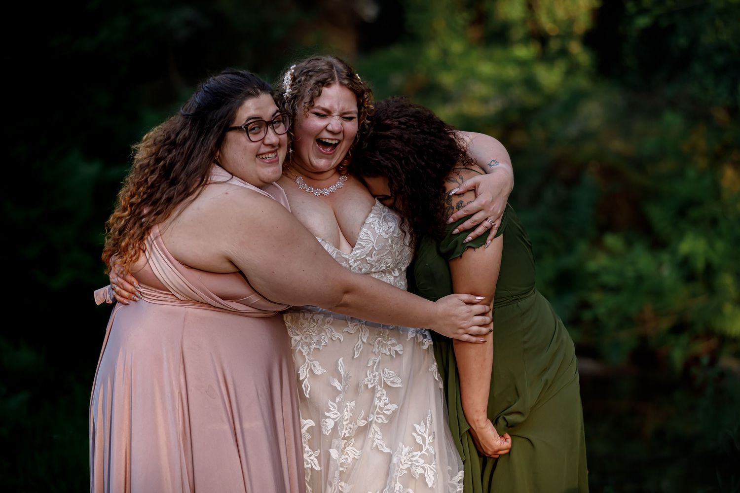 Wedding party members share joyful embraces in light pink and white dresses.