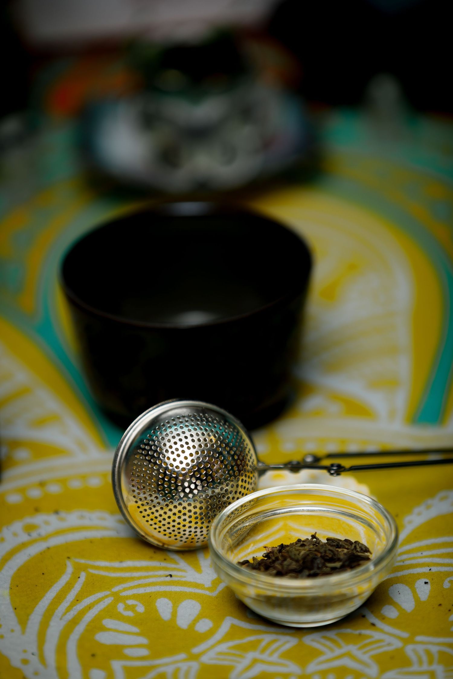 Tea strainer and loose tea leaves on yellow patterned tablecloth.