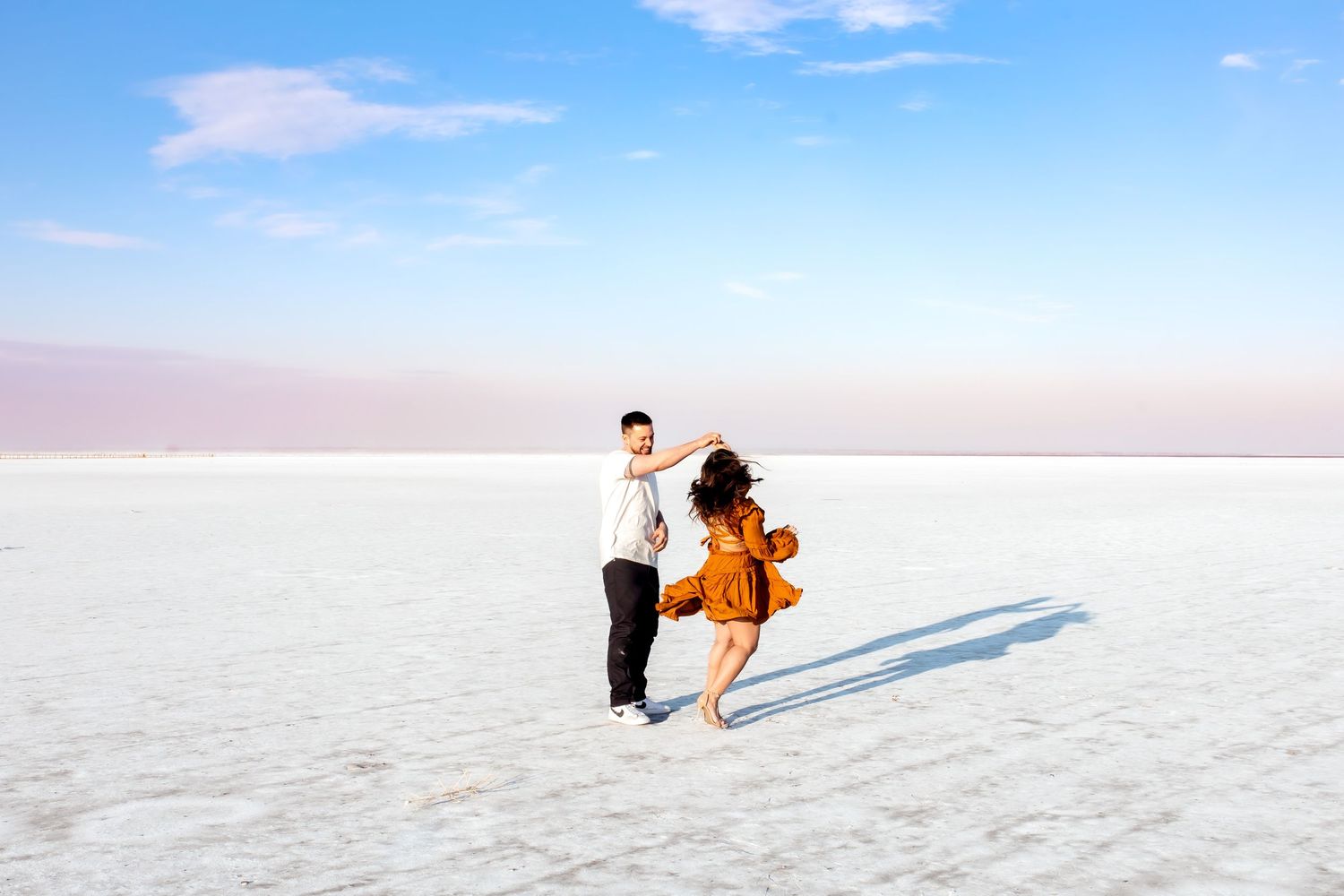 Engagement session on vast white salt flats at sunset under pink and blue skies with an engaged couple where the man is twirling the woman.