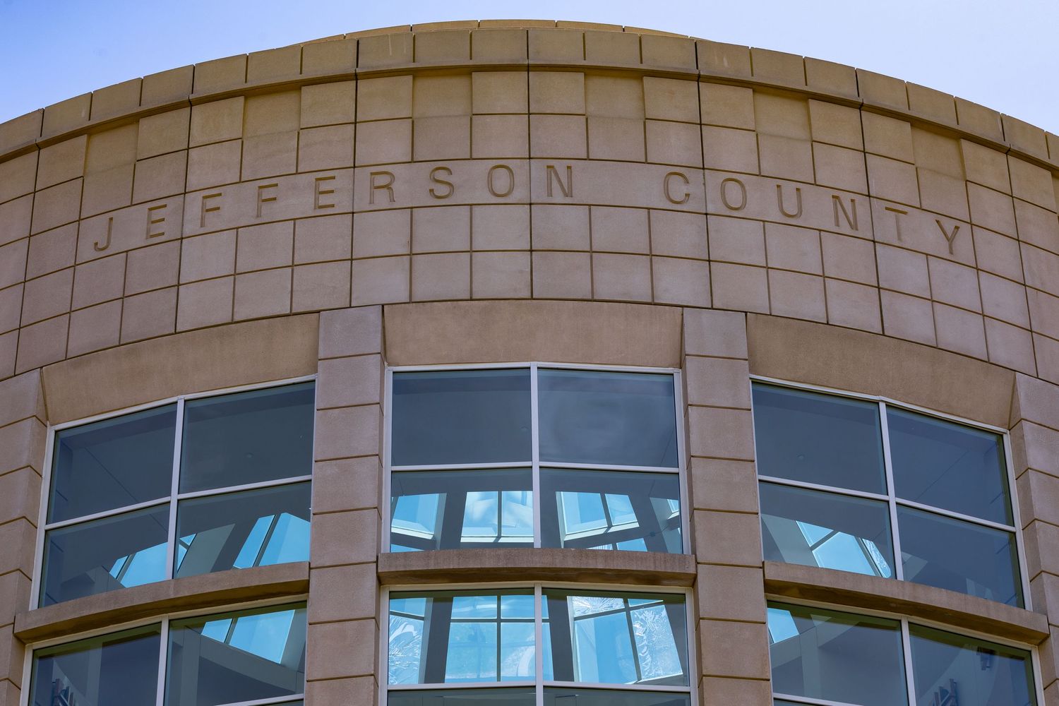 Jefferson County building entrance with curved stone facade and windows reflecting sky.