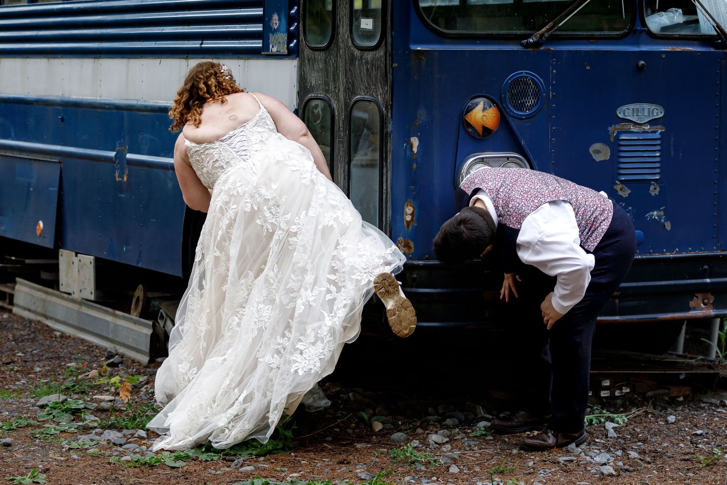 Wedding photo session featuring vintage blue buses as a backdrop in a wooded area.