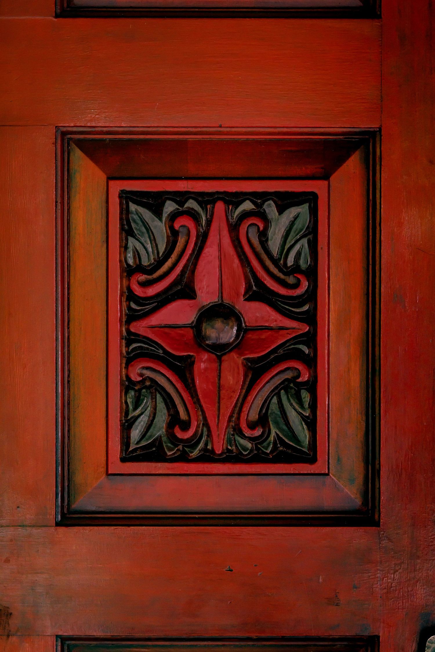 Close-up of an ornate red door panel featuring carved floral patterns and geometric designs.