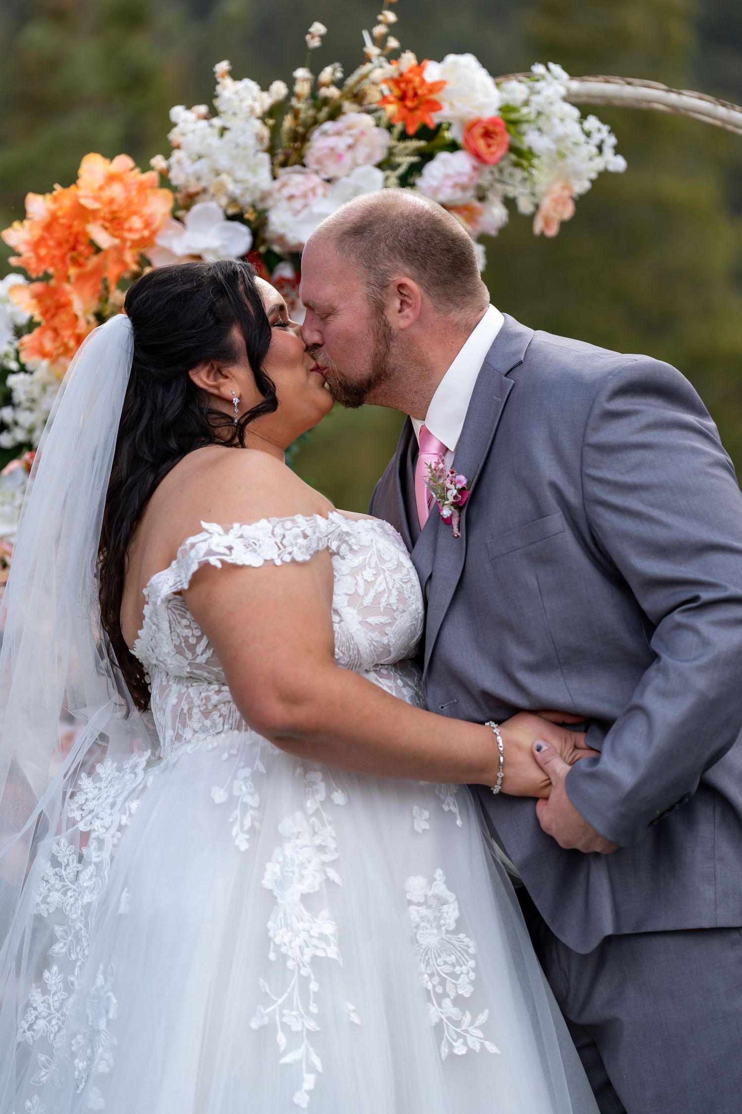 Romantic wedding kiss sequence under floral arch with orange and white flowers.