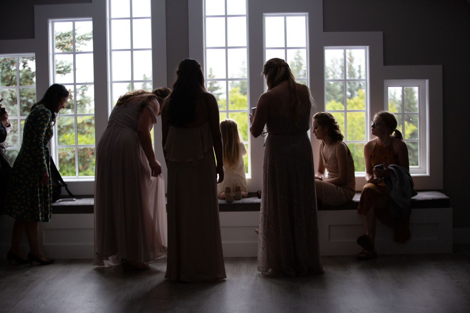 Silhouettes of wedding guests standing by large windows in a dim room.