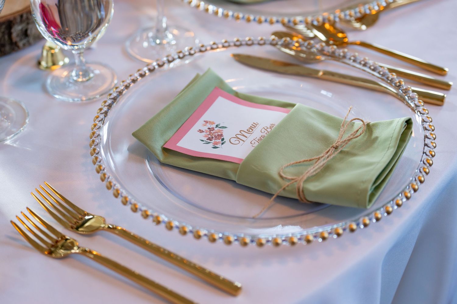 Formal place setting with beaded charger plate, mint napkin, and gold flatware.