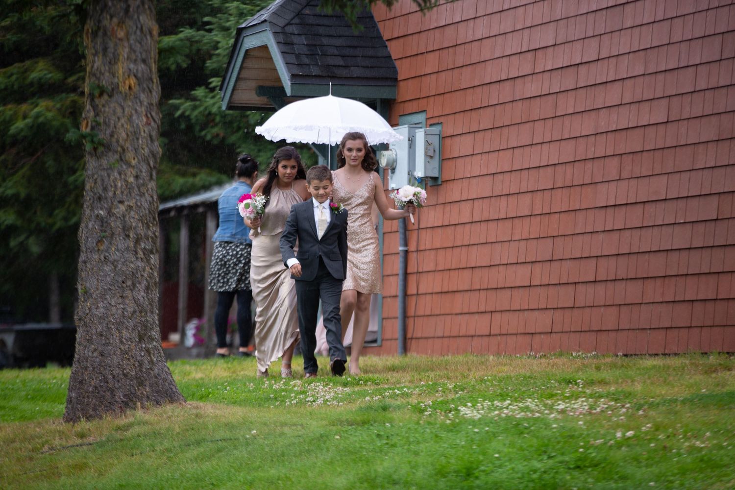 Wedding guests walking on a grassy hill beside a brick building.