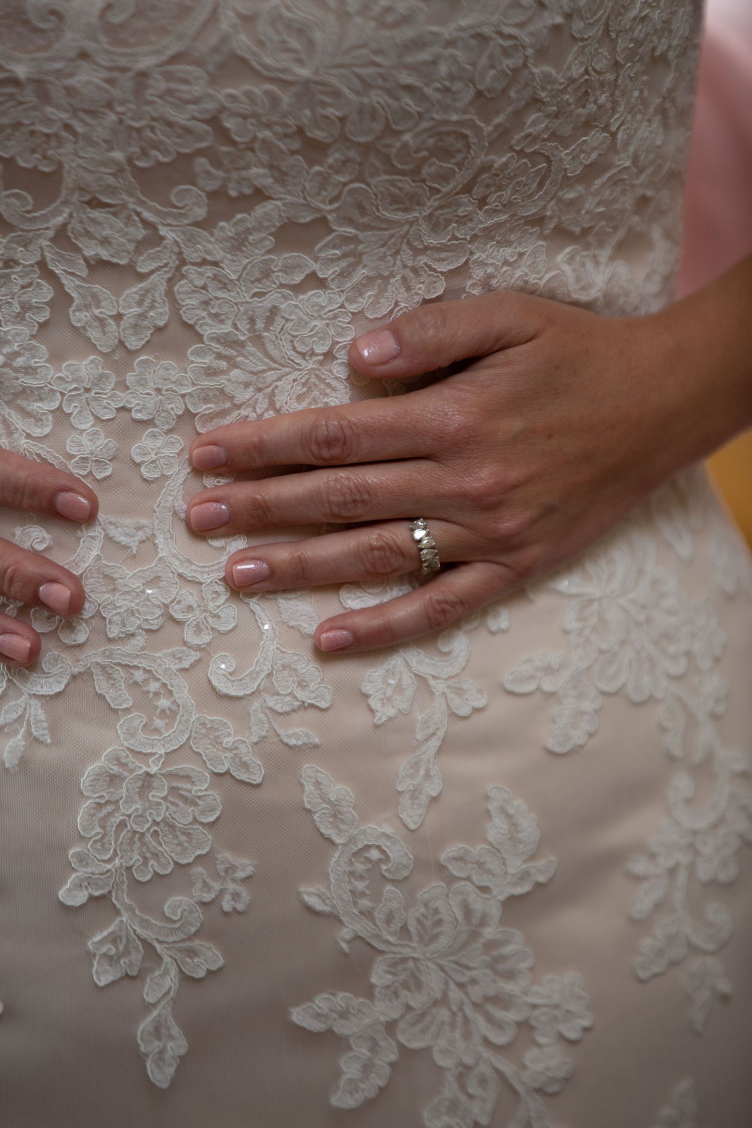 Detail of delicate white lace pattern on a wedding dress with hands gently touching the fabric.