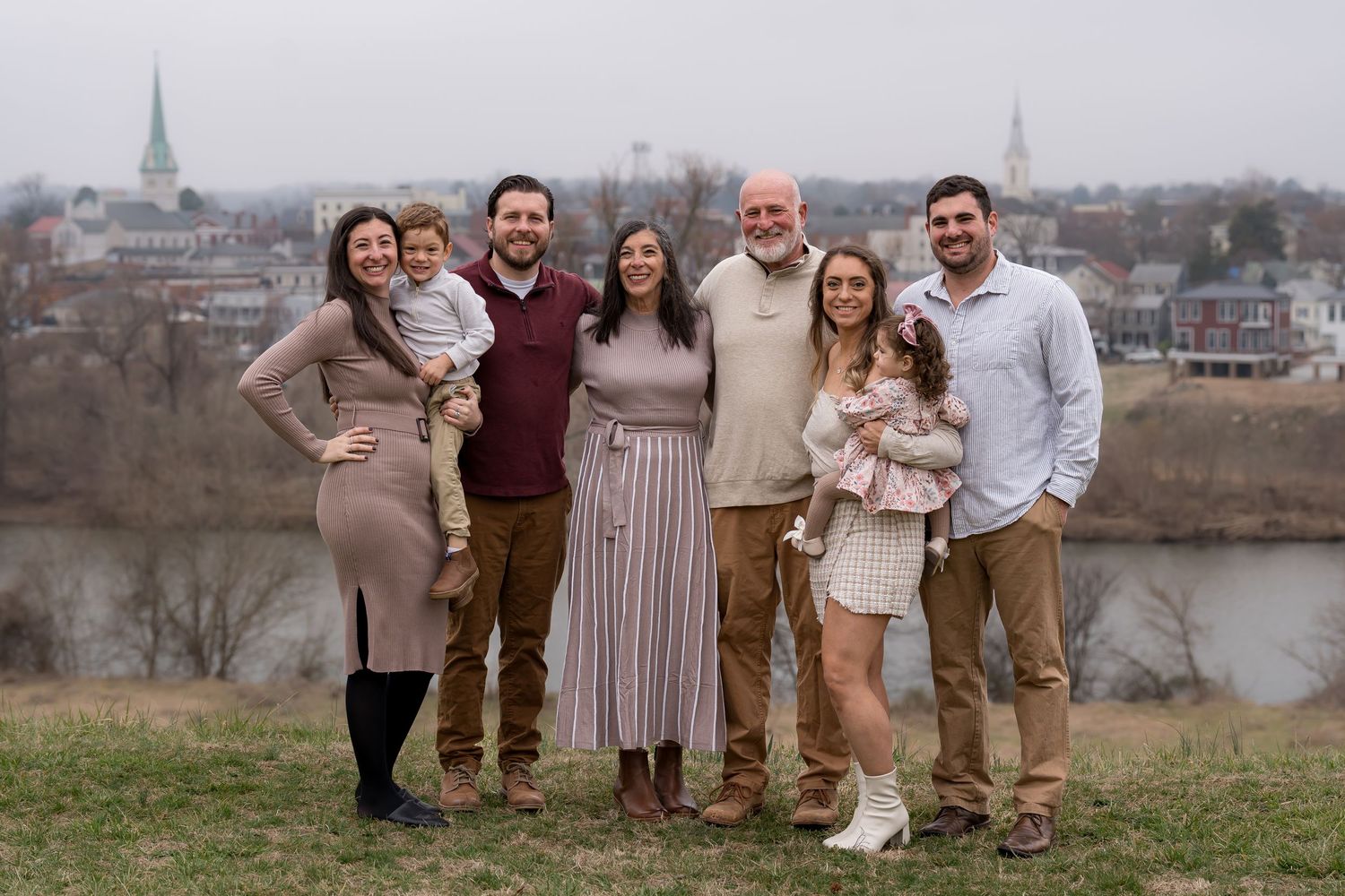 Extended family gathering for outdoor photos with urban landscape in background.