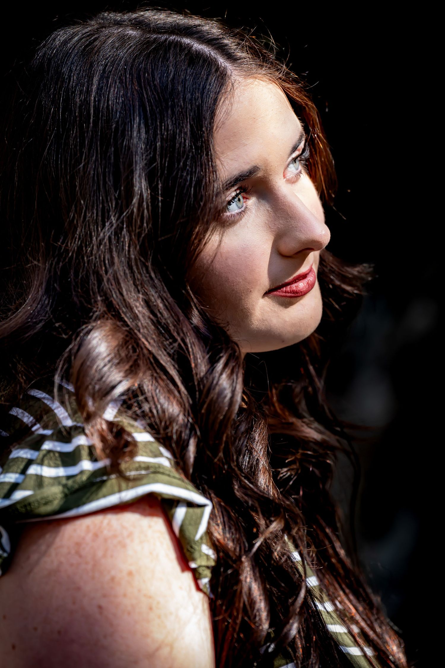 Dramatic lighting portrait with dark background highlighting wavy hair and striped clothing.