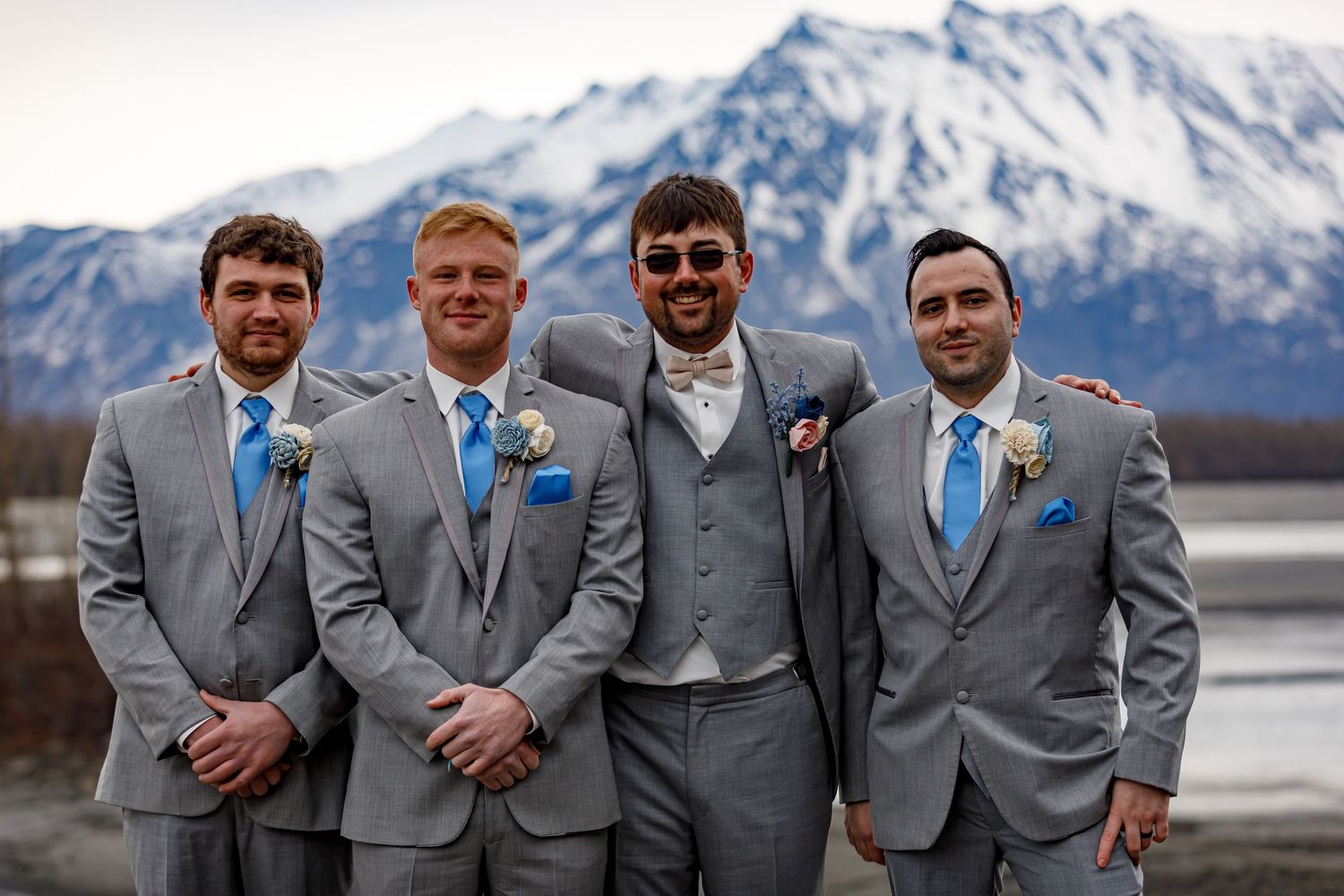 Groomsmen in matching grey suits pose with snow-covered mountains behind them.