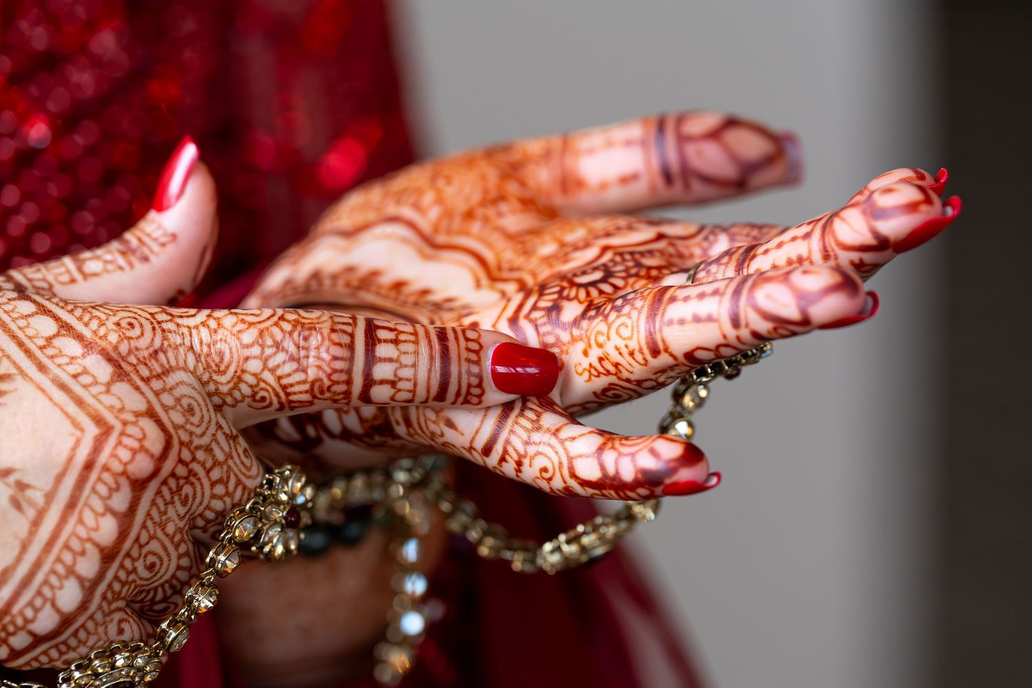 Intricate red henna designs adorning hands with jewelry accents.