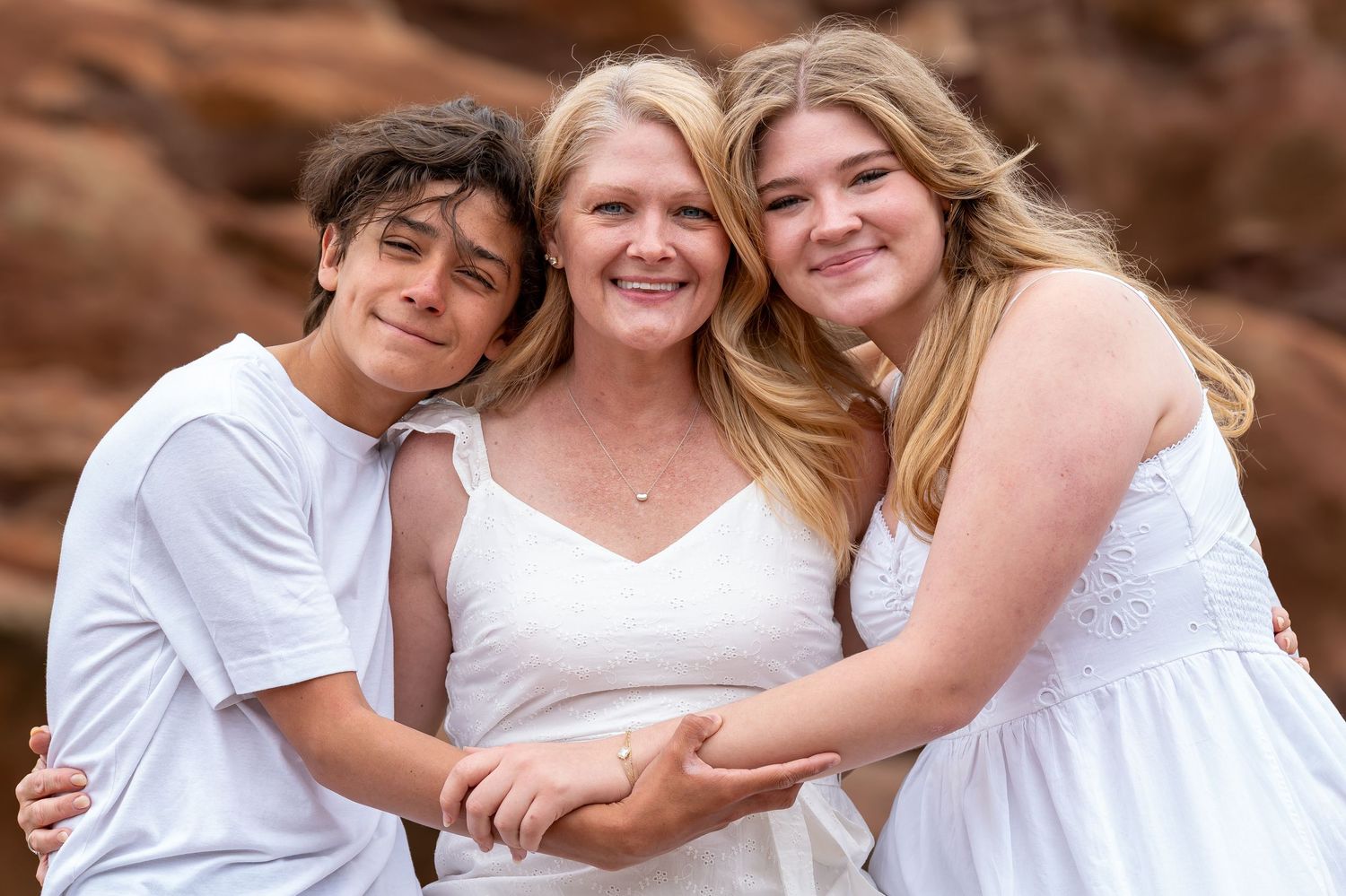 Family group hugging and smiling together against red rock formations.