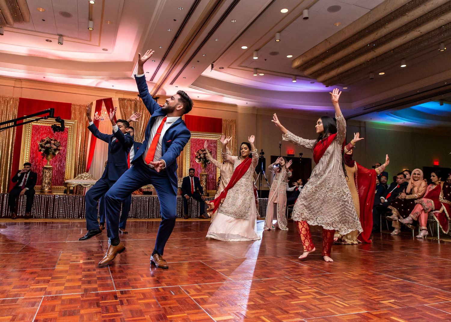 Wedding guests performing synchronized dance moves on a wooden dance floor.