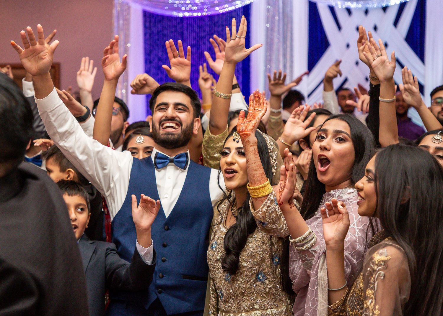 Energetic wedding reception guests dancing with hands raised in celebration.