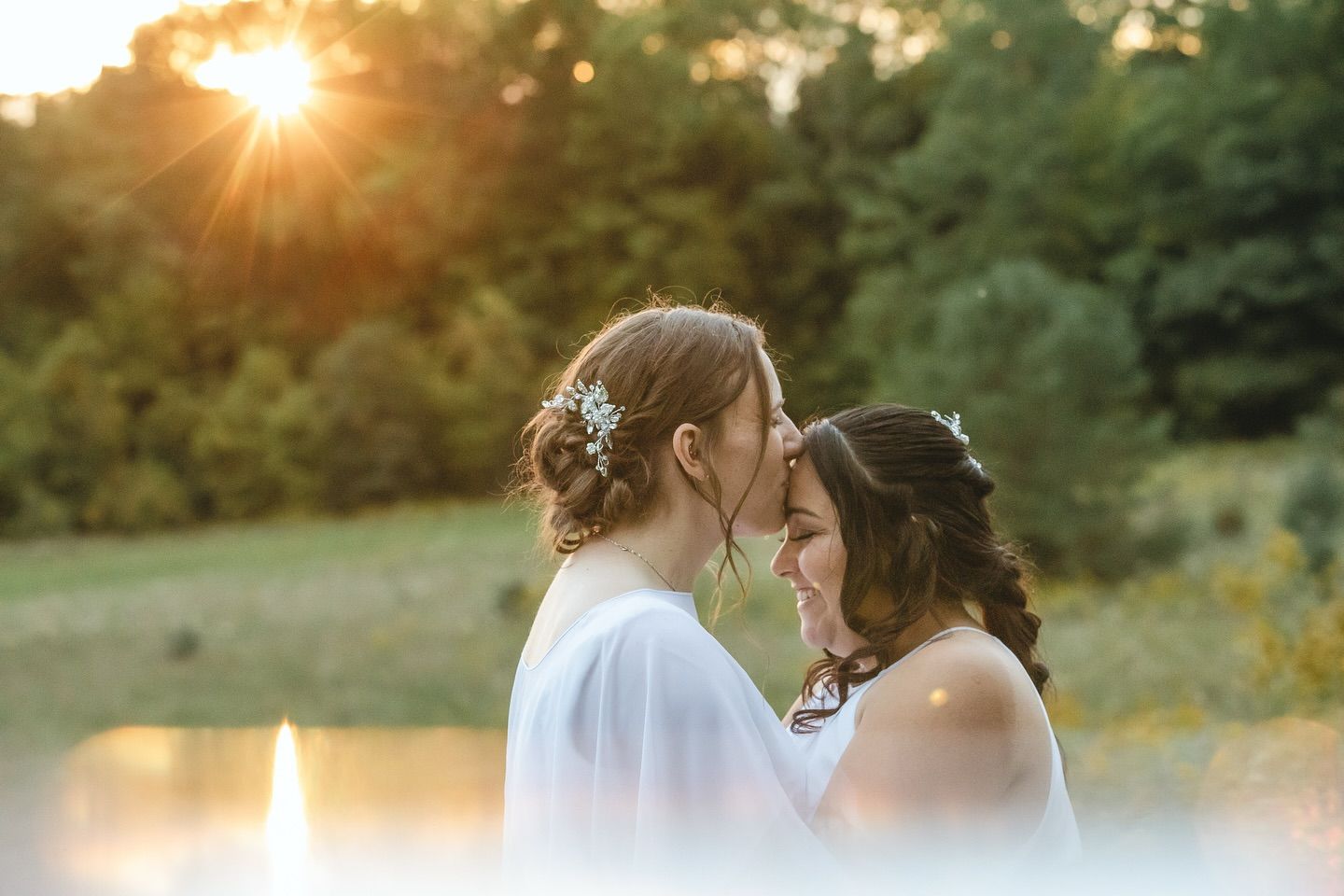 Intimate wedding moment captured during golden hour with sun flare in background.