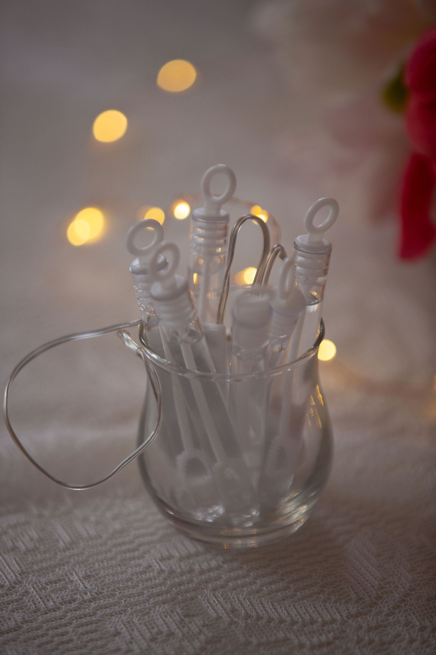 White bubble wands arranged in a clear glass vase with soft bokeh lights in the background.