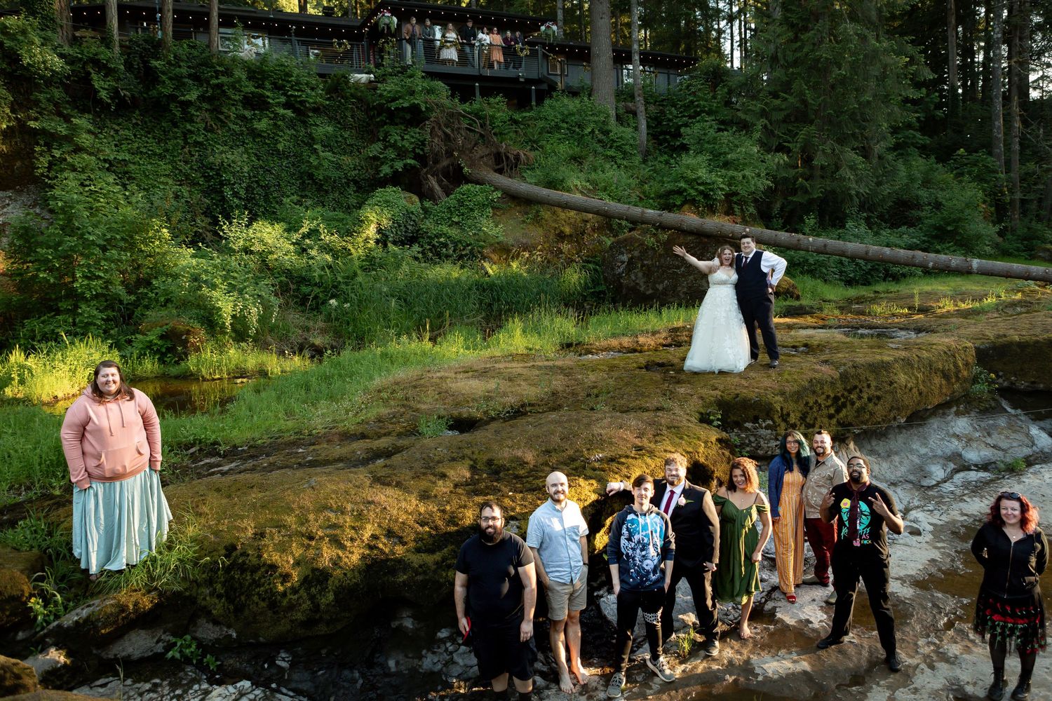 Wedding party and guests gather outdoors in forest setting.