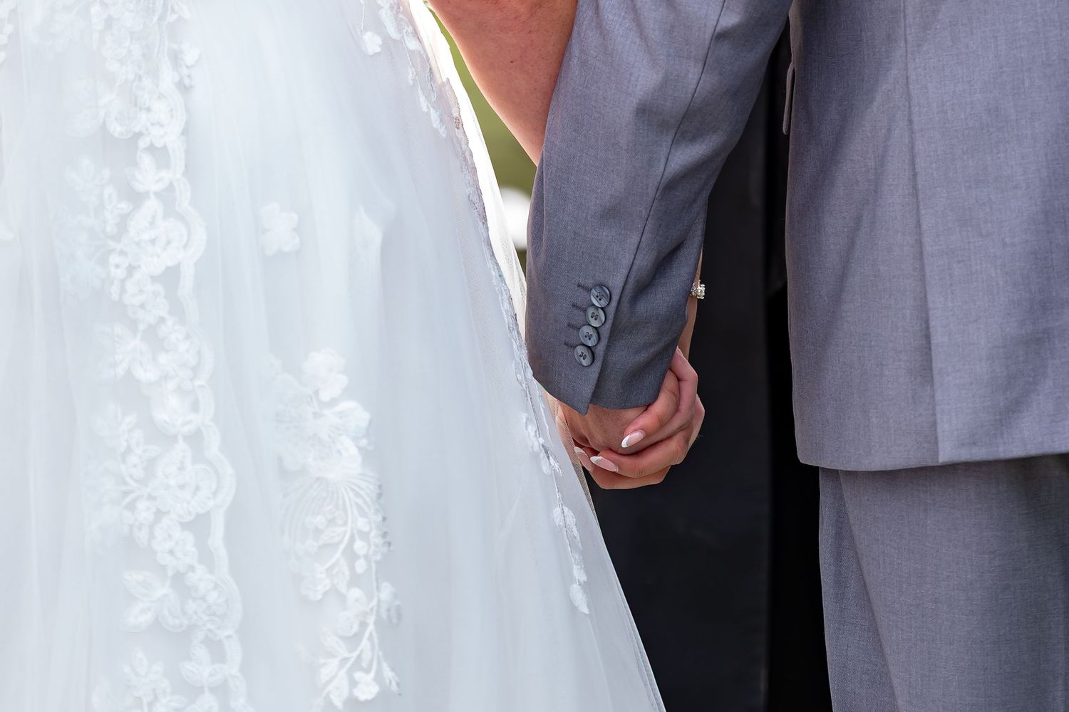 Detail shot of white lace wedding dress and gray suit during outdoor ceremony.