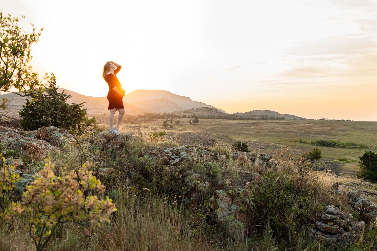 Silhouette of a figure standing on a rocky outcrop against a golden sunset over rolling hills.
