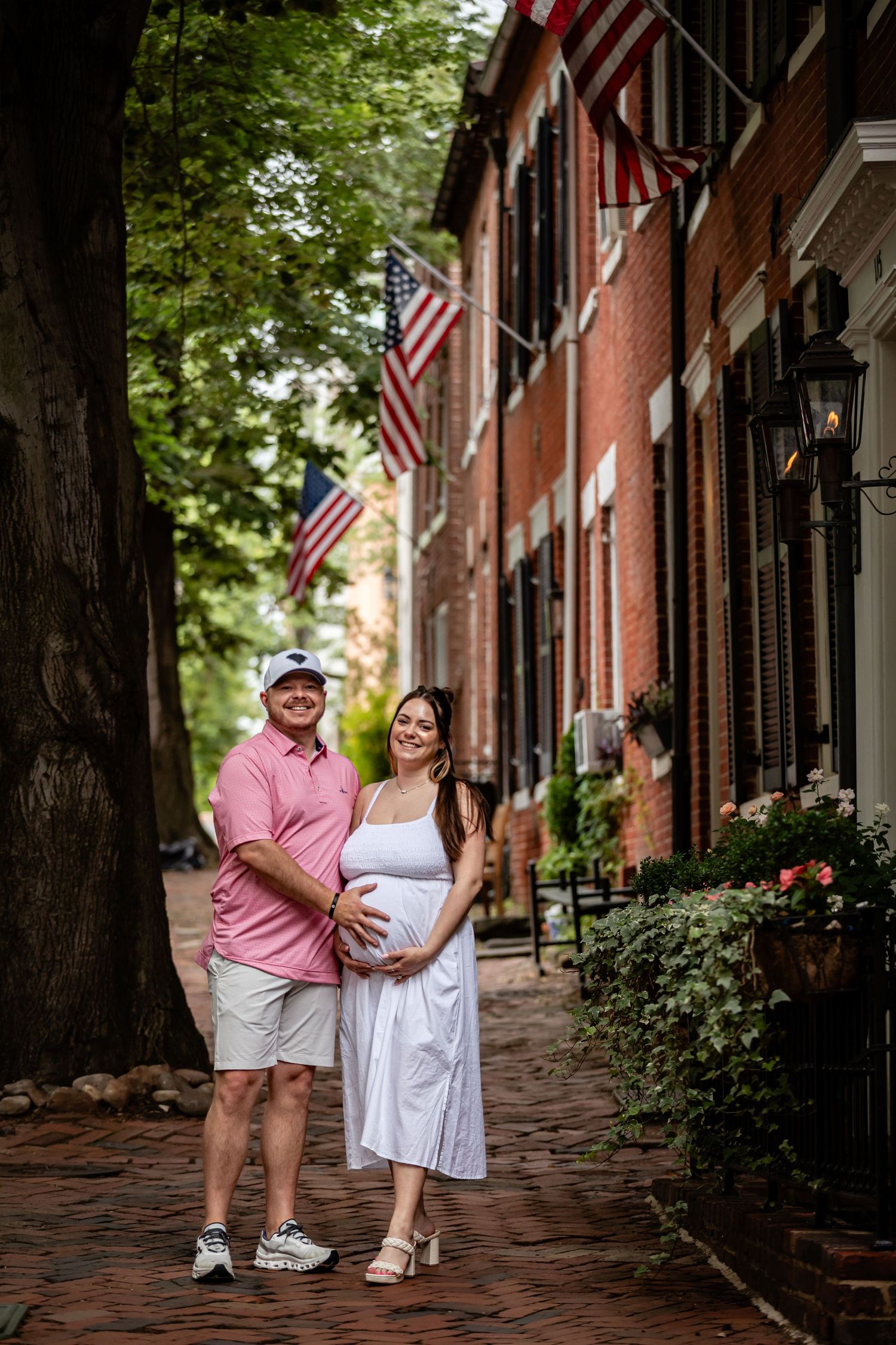 Two people stand together on a historic brick-lined sidewalk with American flags decorating the buildings.
