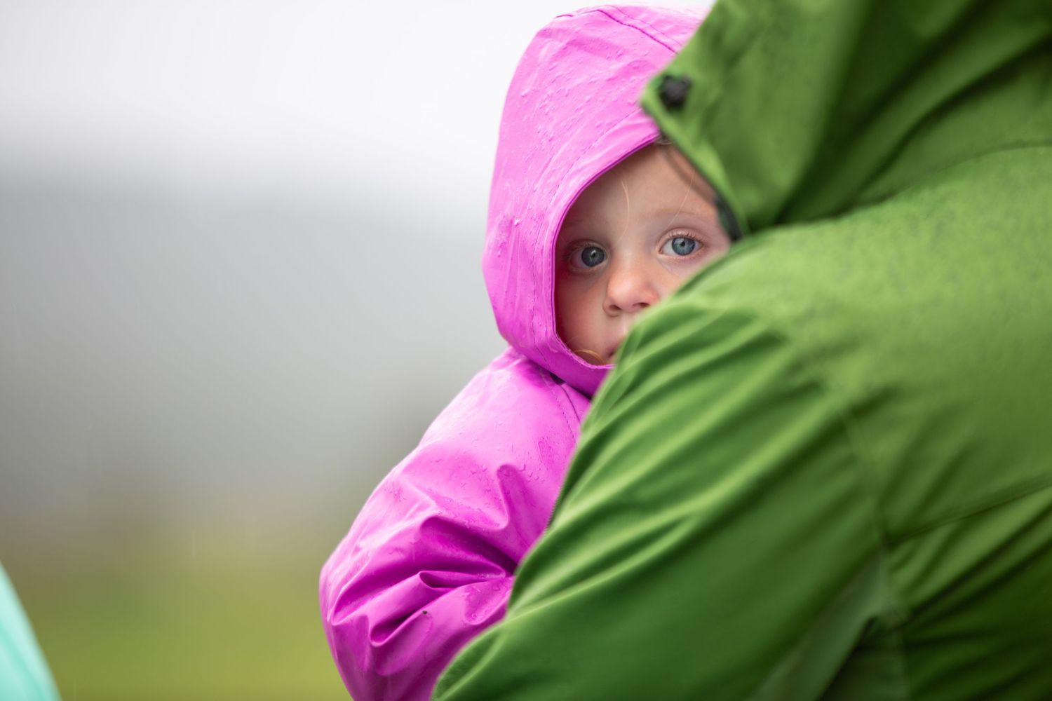 Close up of someone wearing a vibrant pink hooded raincoat against a green natural background.