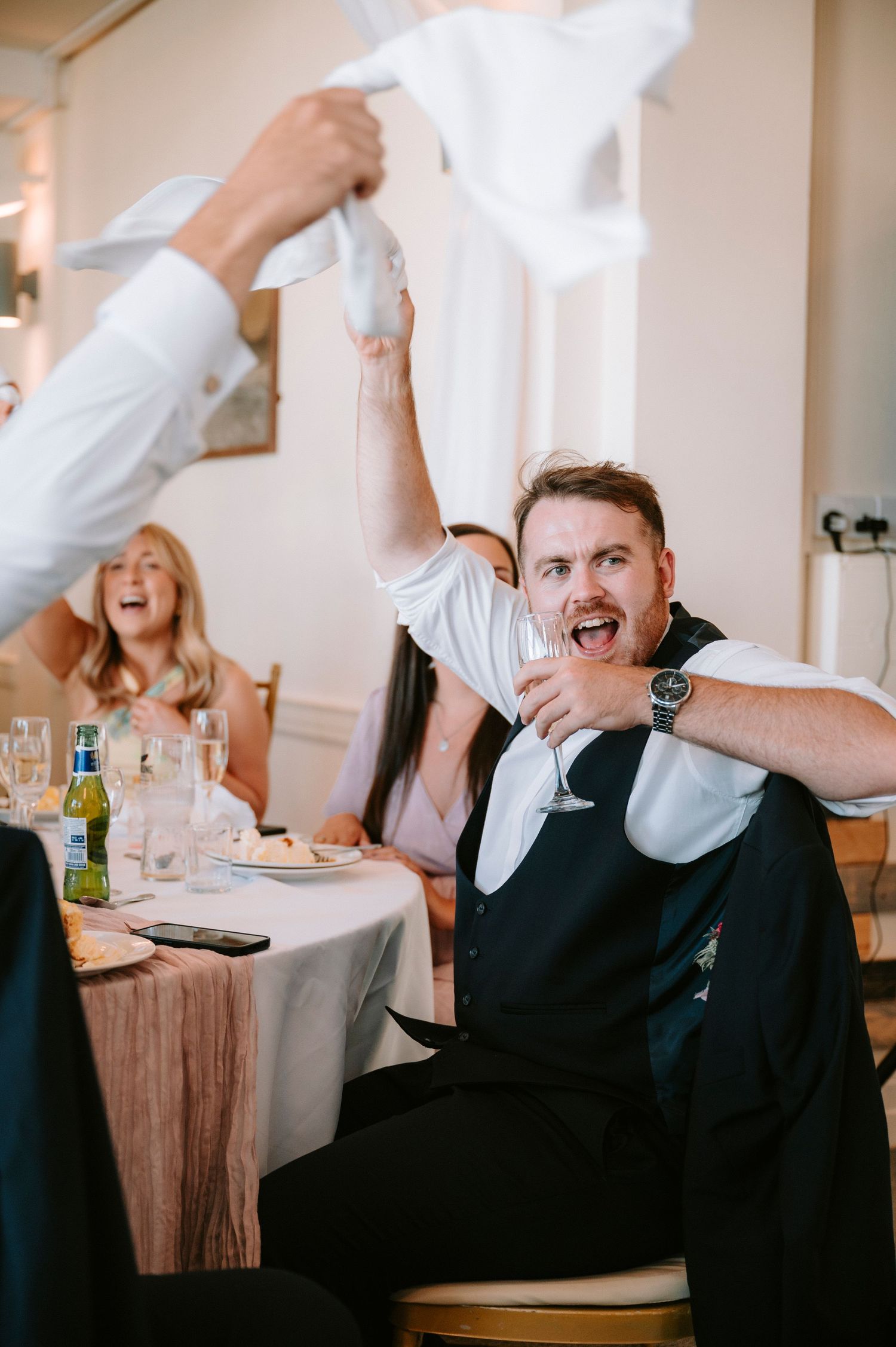 Wedding guests wave white napkins while celebrating at decorated reception tables.