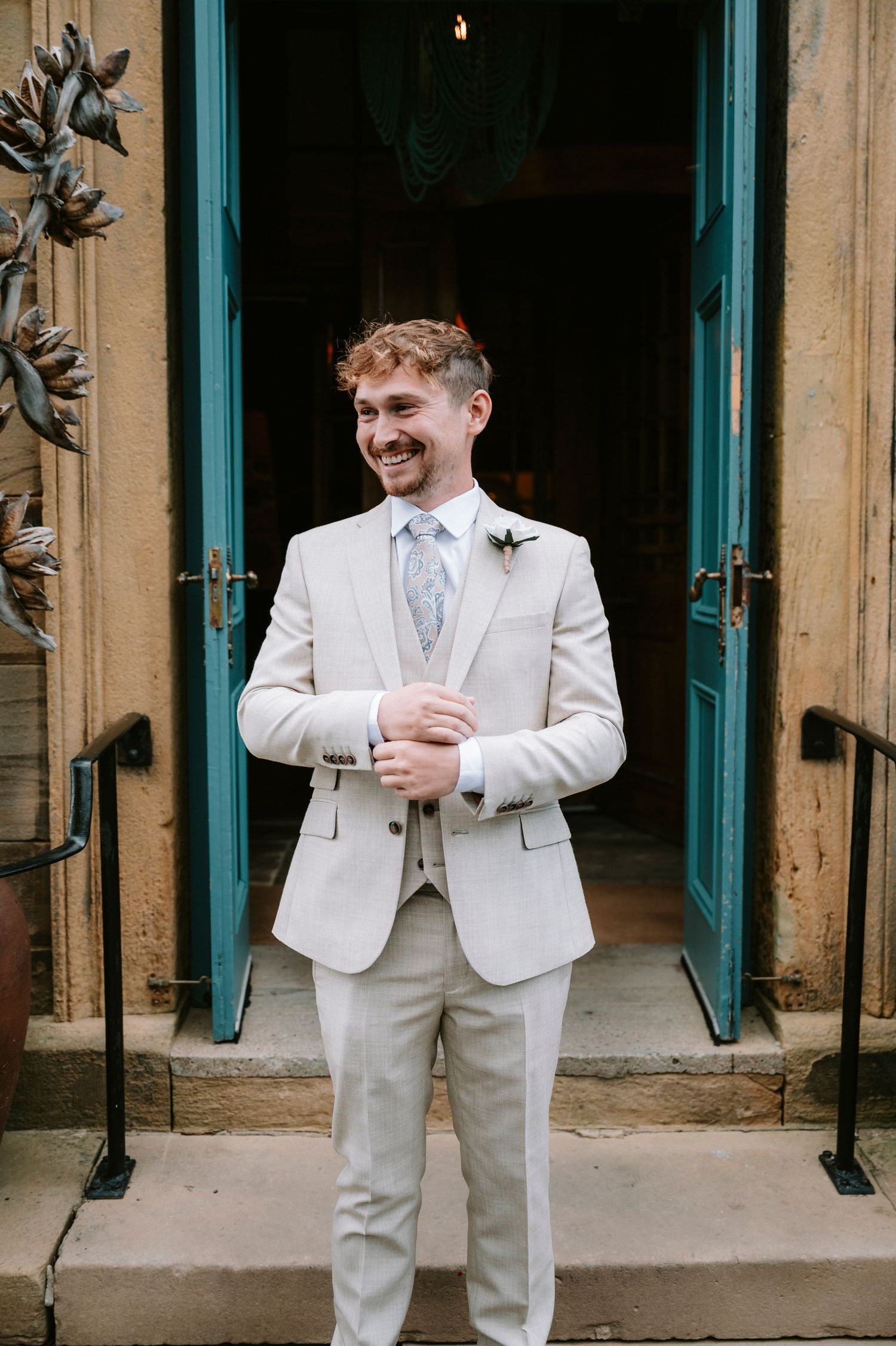 Groomsmen in light beige suits pose against turquoise doors of historic building.