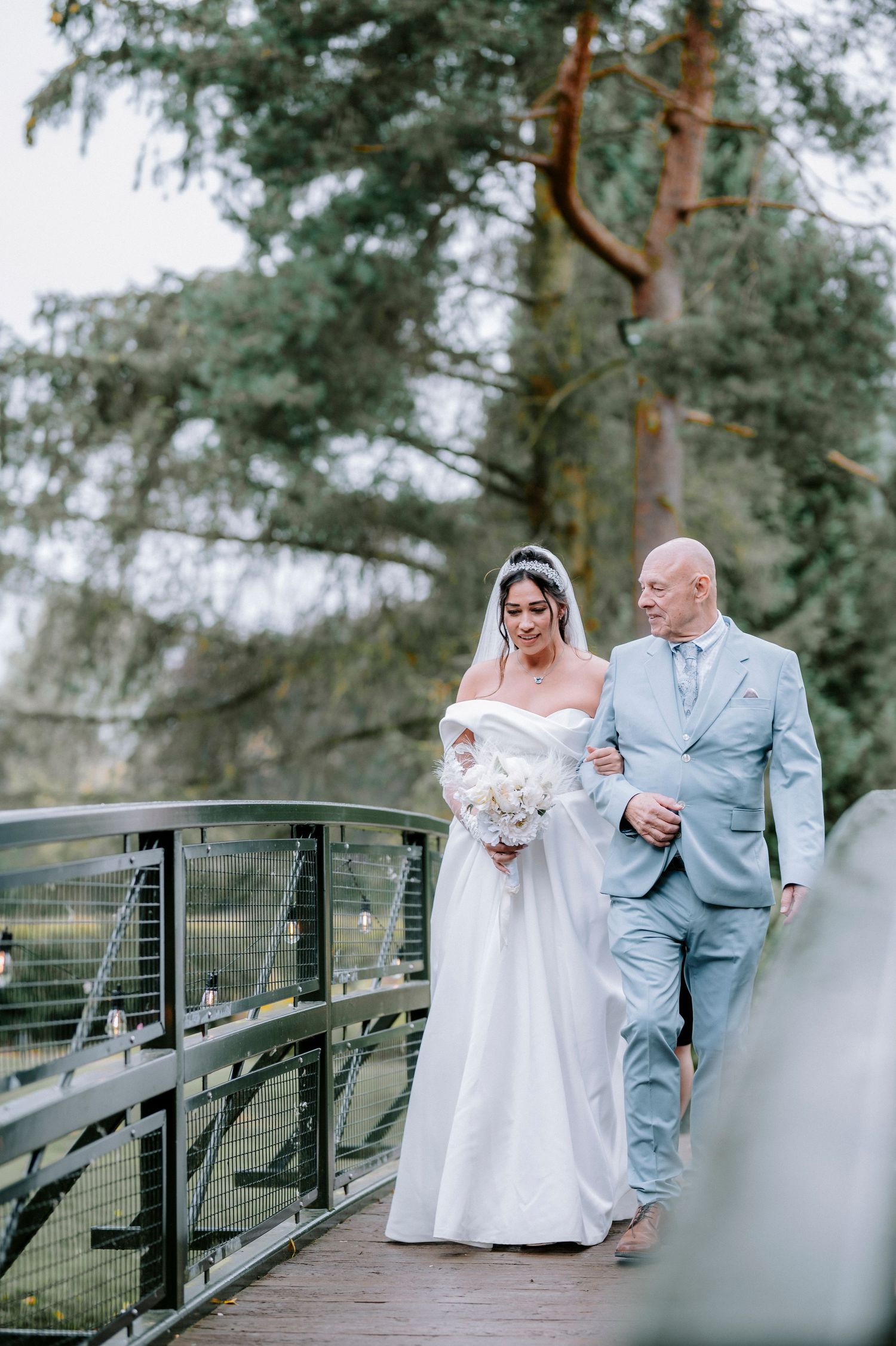 Couple poses on a rustic wooden bridge surrounded by evergreen trees during their wedding photoshoot.