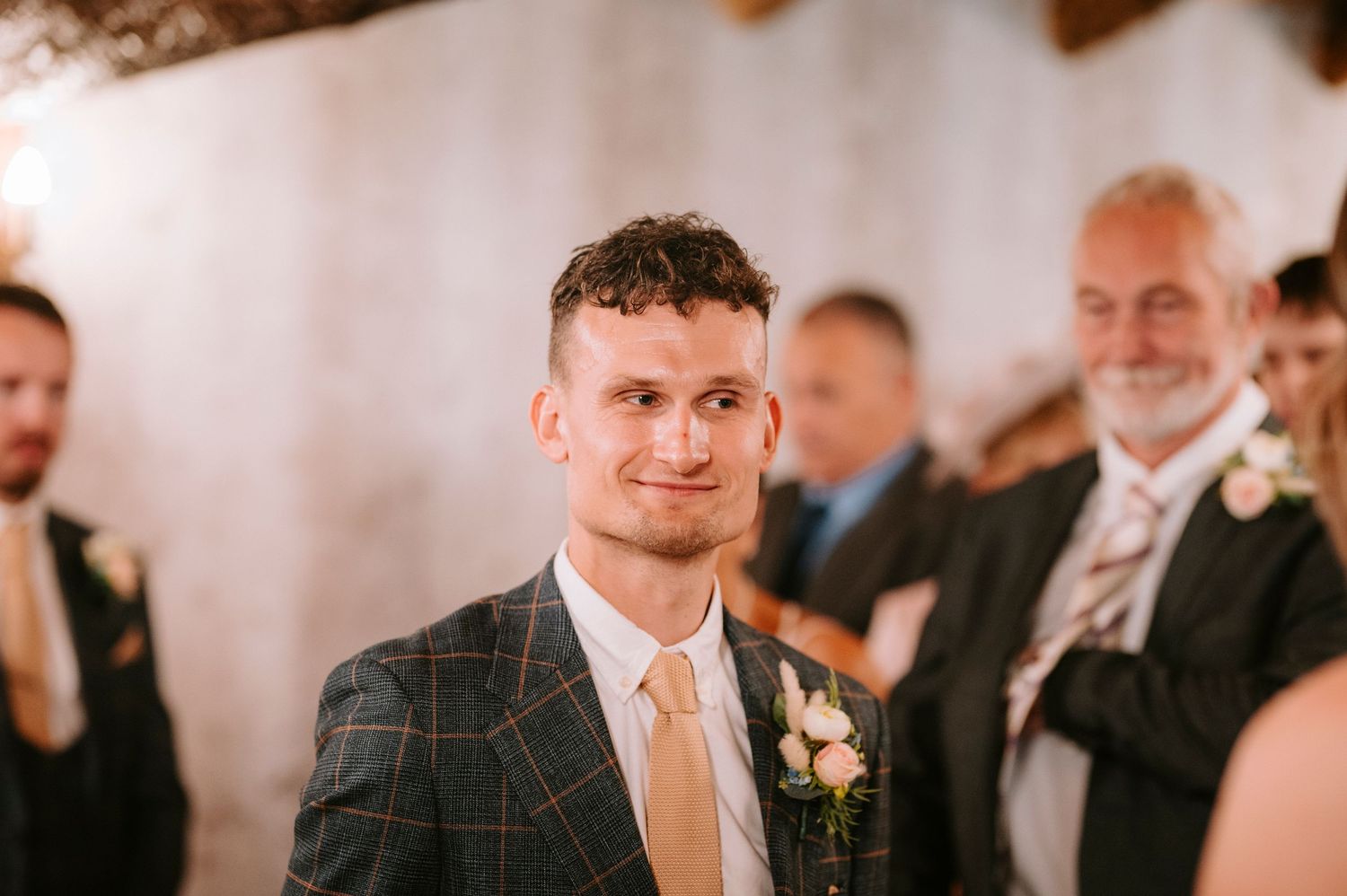 A wedding guest in a checkered suit and champagne tie smiles during the celebration.