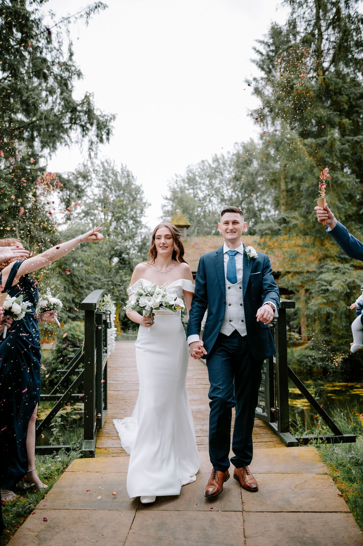 Wedding celebration with confetti toss on outdoor wooden deck surrounded by trees.