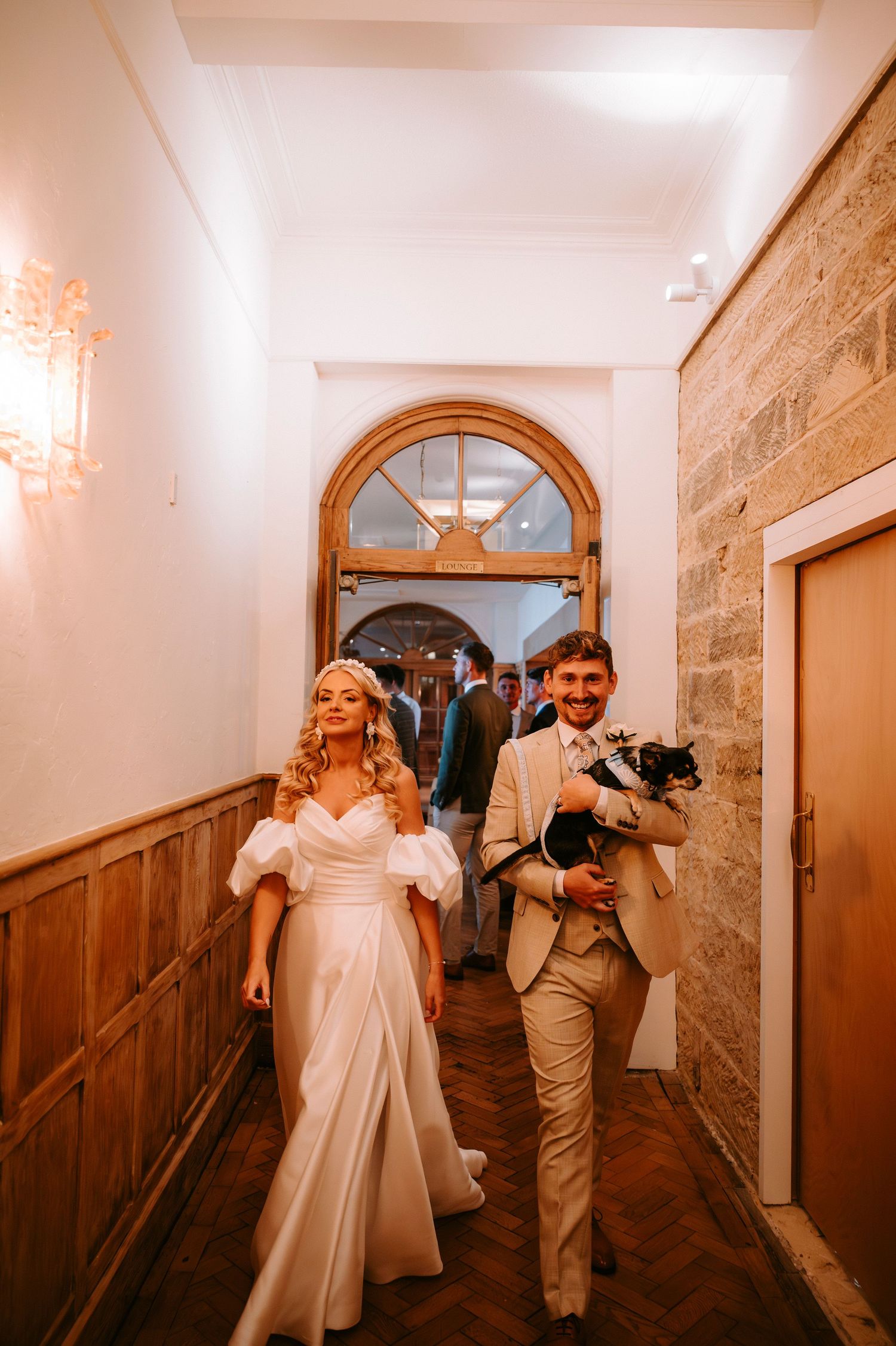 Couple walks through an elegant hallway with wooden paneling and arched windows during their wedding.