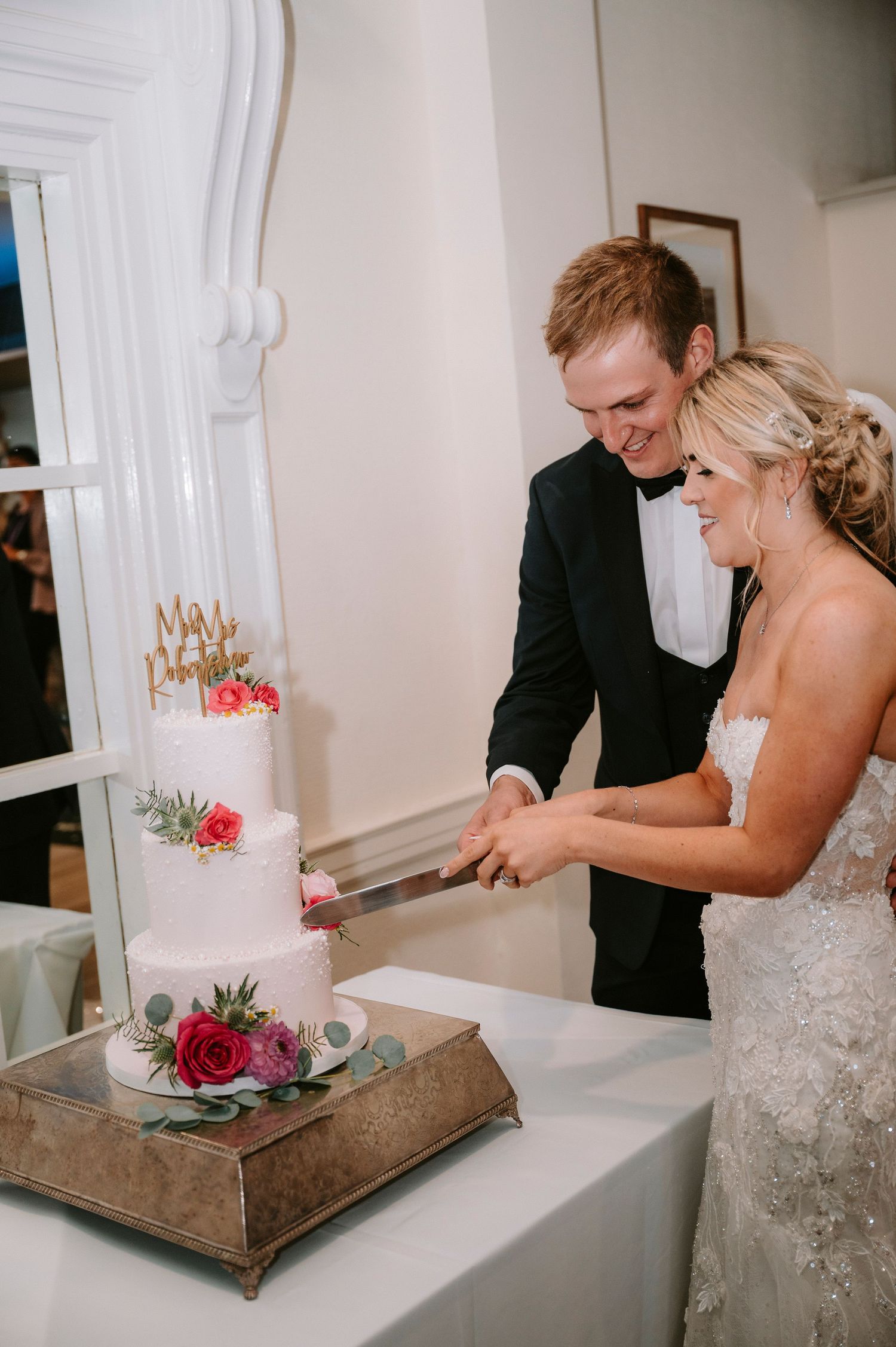 Newlyweds cut their elegant white wedding cake together during their reception celebration.