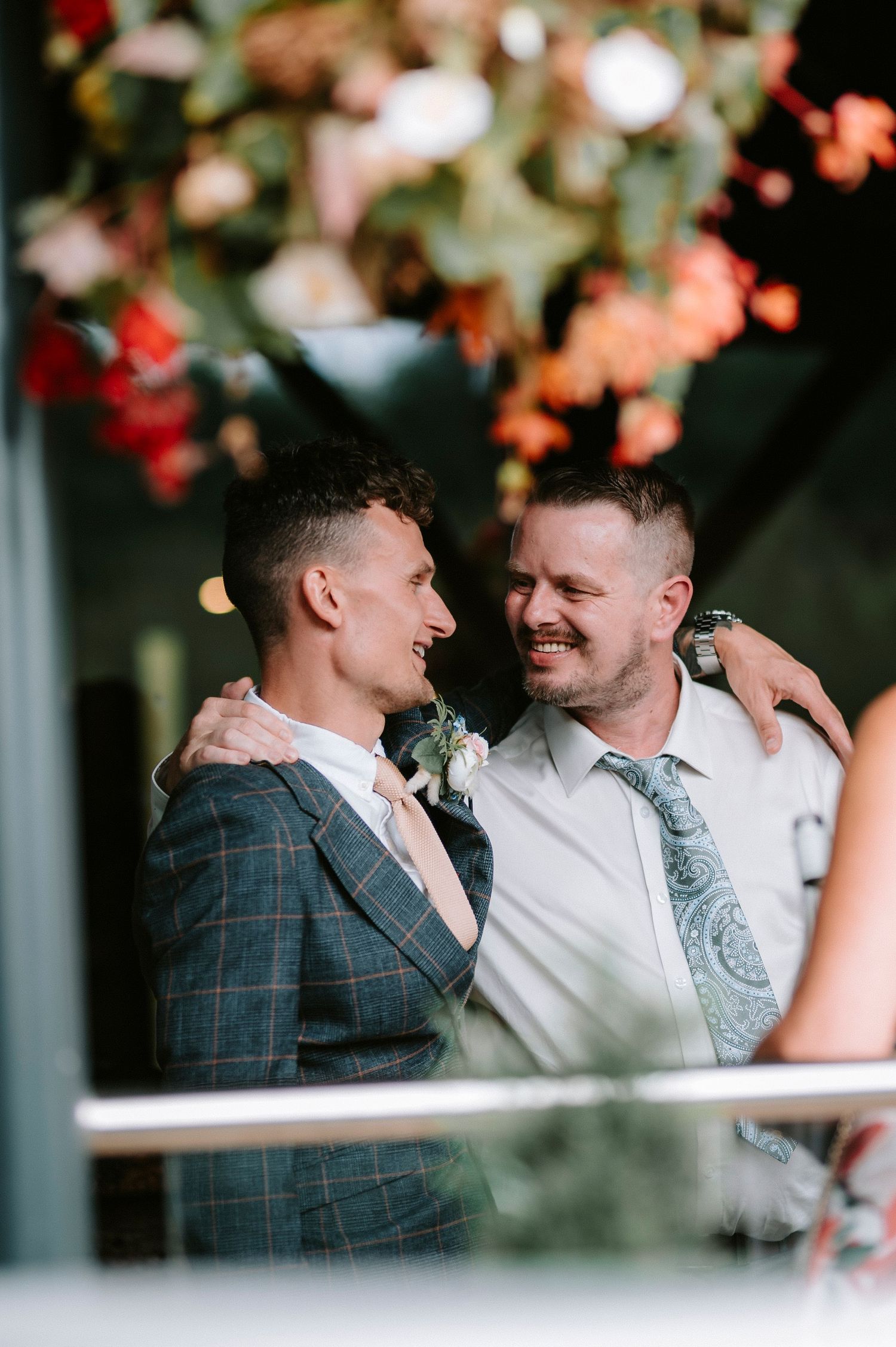 Two wedding guests share a joyful moment under floral decorations at an outdoor celebration.