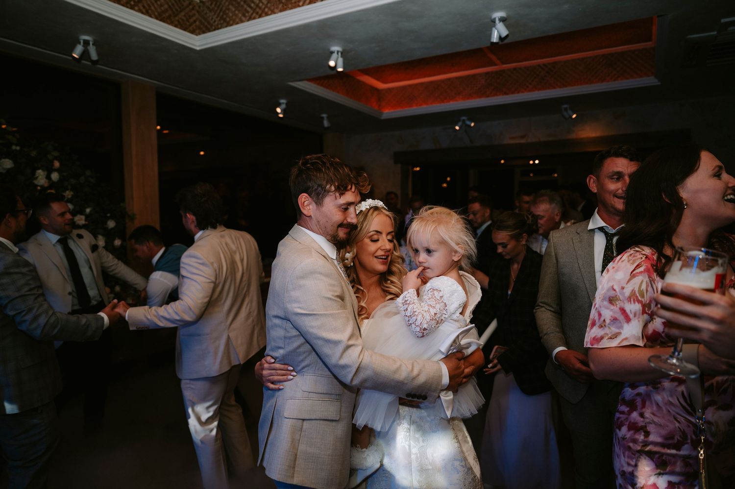 Wedding guests dancing and celebrating at an indoor reception with ambient lighting.