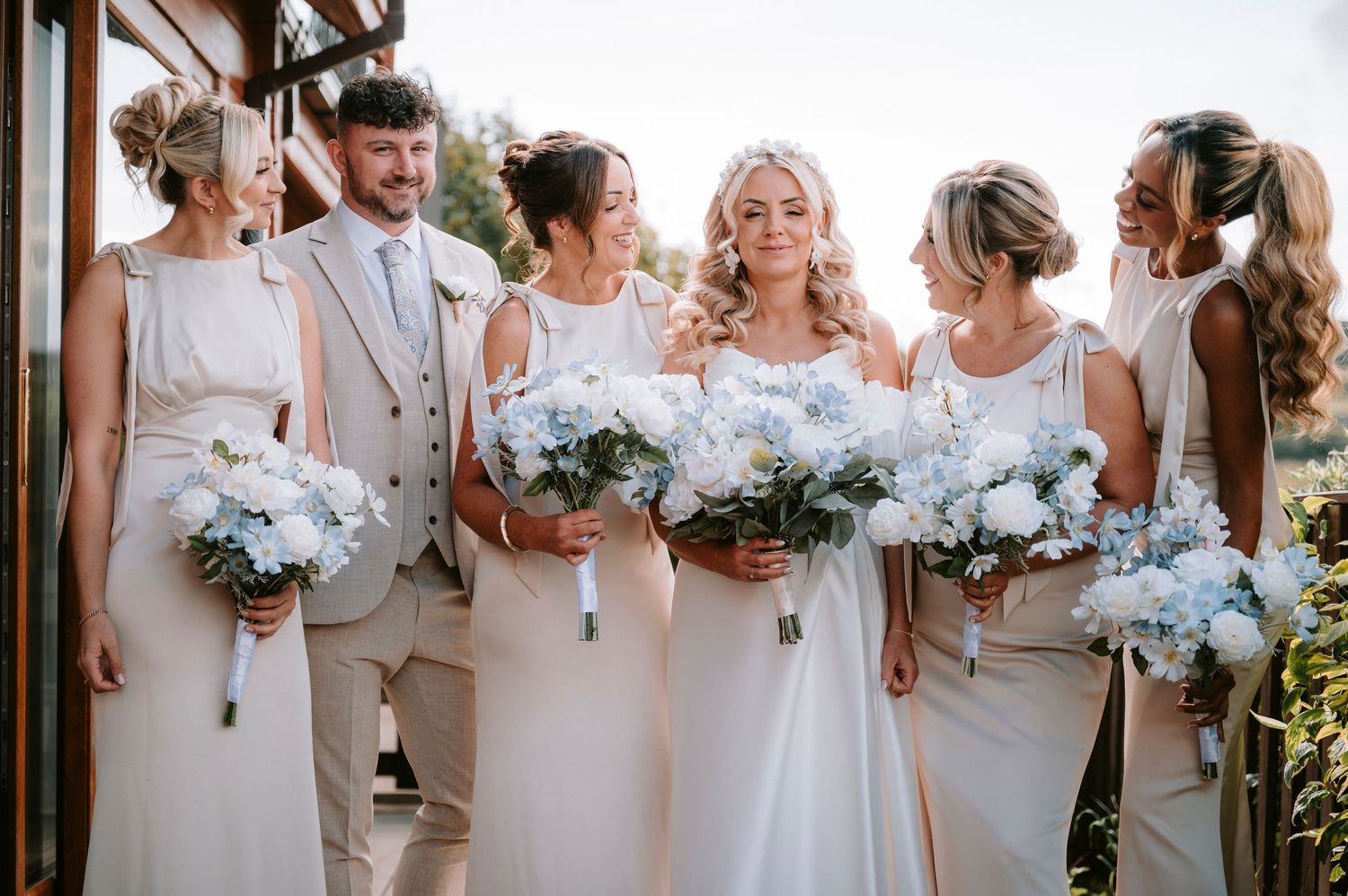 Wedding party in neutral beige and white attire holding bouquets of white flowers.