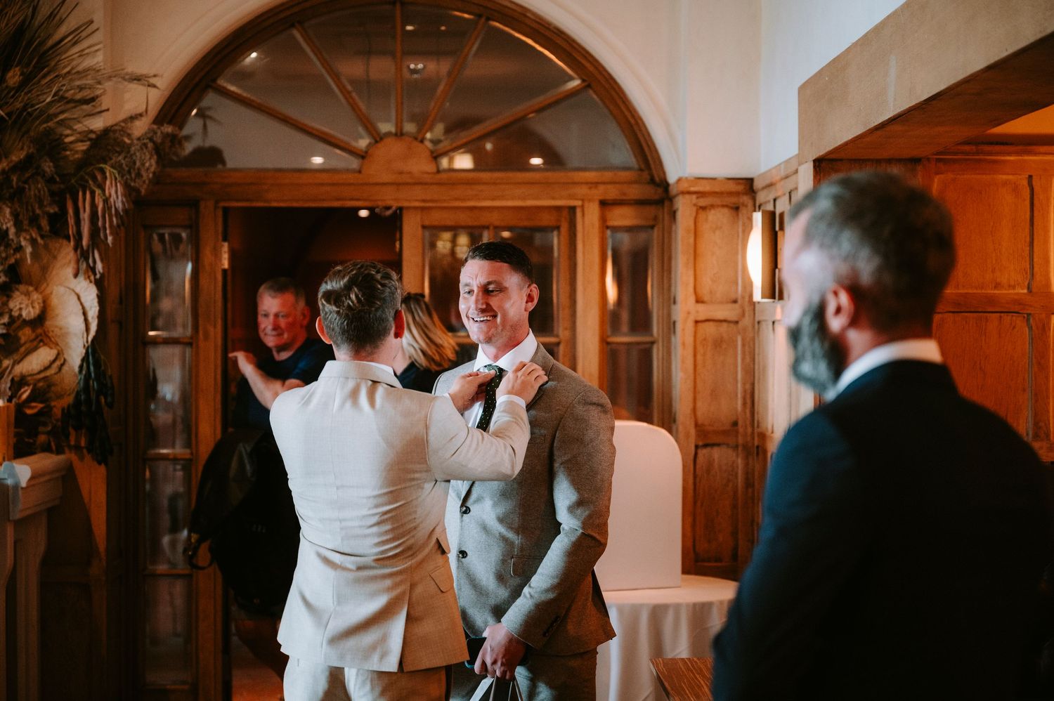 Wedding party members in formal attire gather in an elegant indoor venue with wooden archways.