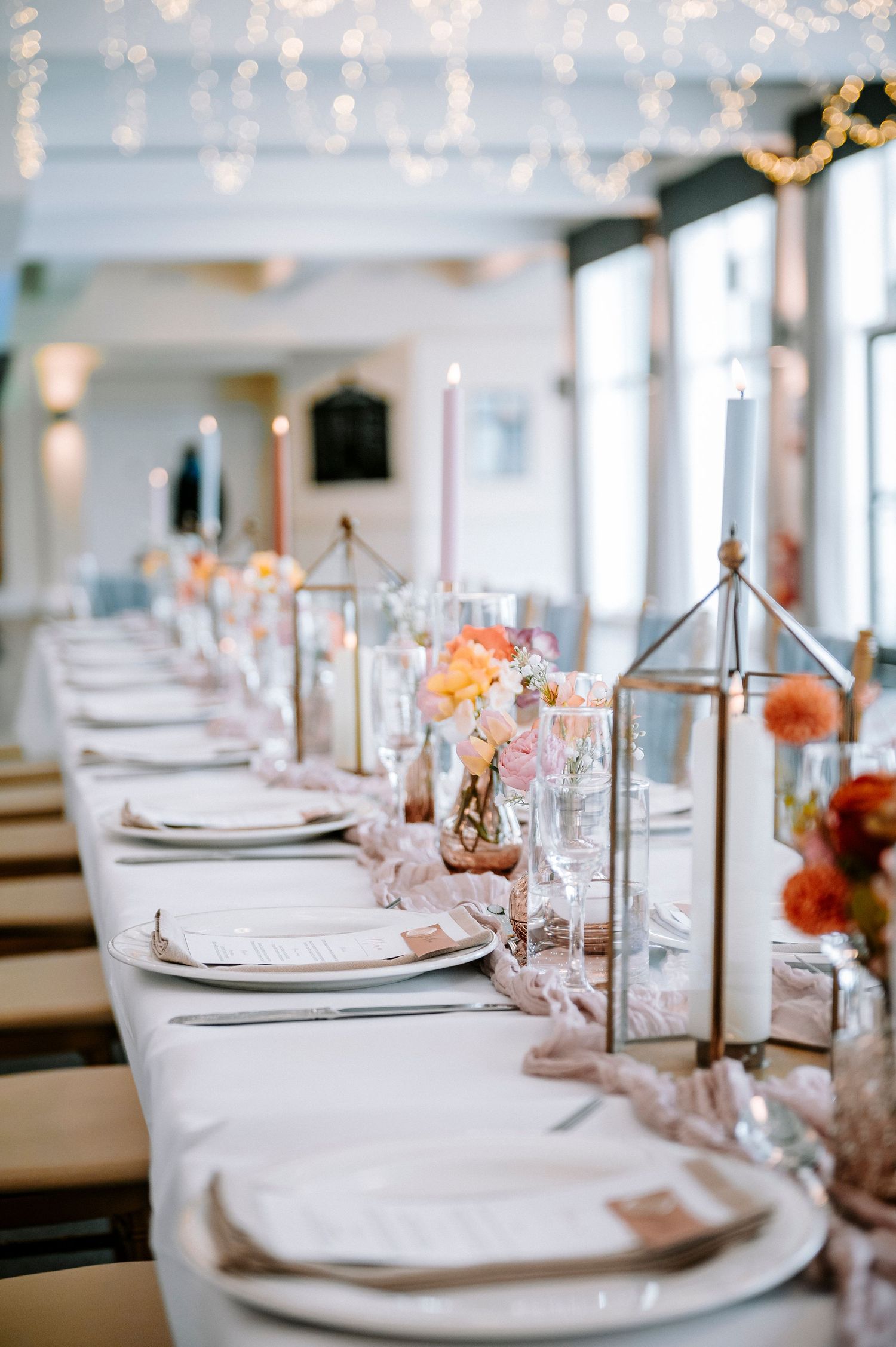 An elegant wedding reception table setting with string lights and peach floral accents.